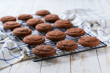 Freshly baked chocolate brownie cookies cooling on a black wire rack, with in a light kitchen table, selective focus.
