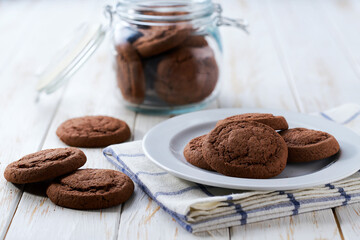 Glass jar with tasty chocolate cookies on a on a white table.