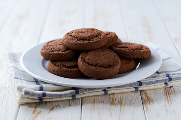 Tasty chocolate cookies in a plate with on a light kitchen table, selective focus.