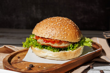 hamburger with green salad, tartar sauce, ketchup, sesame bun, on a dark background with sauces, fast food, snack
