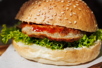hamburger with green salad, tartar sauce, ketchup, sesame bun, on a dark background with sauces, fast food, snack