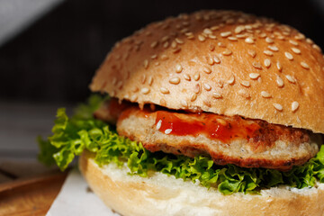 hamburger with green salad, tartar sauce, ketchup, sesame bun, on a dark background with sauces, fast food, snack