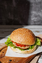 hamburger with green salad, tartar sauce, ketchup, sesame bun, on a dark background with sauces, fast food, snack