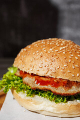 hamburger with green salad, tartar sauce, ketchup, sesame bun, on a dark background with sauces, fast food, snack