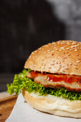 hamburger with green salad, tartar sauce, ketchup, sesame bun, on a dark background with sauces, fast food, snack
