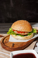hamburger with green salad, tartar sauce, ketchup, sesame bun, on a dark background with sauces, fast food, snack