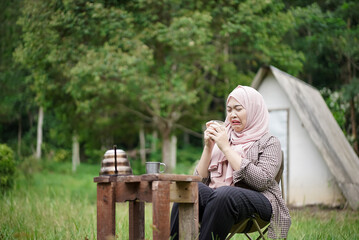 Naklejka premium young Indonesian woman in hijab enjoying a cup of black coffee while enjoying the beauty and relaxing atmosphere of nature, travel concept.