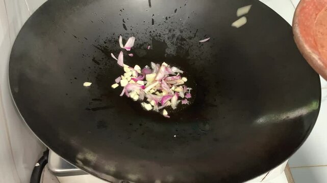 A close-up of a wok with oil and chopped garlic, ready for cooking.