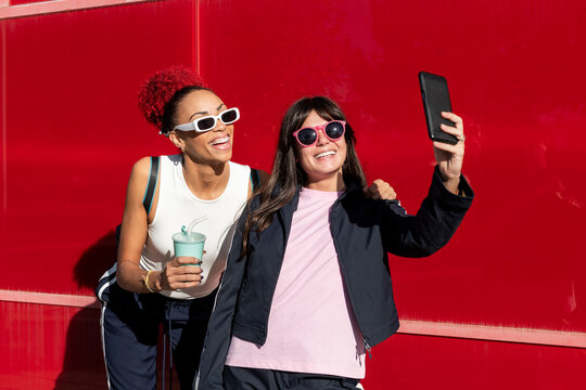 Young friends taking selfie through smart phone near red background