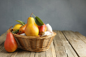 Ripe juicy pears in wicker basket on wooden table against grey background