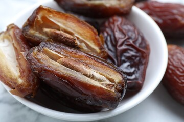 Many tasty dried dates in bowl on light table, closeup