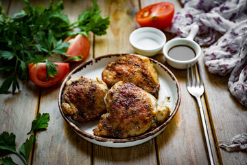 Grilled chicken thighs on a white plate on a wooden table. Home cooking: fried chicken thighs for lunch. Close-up.