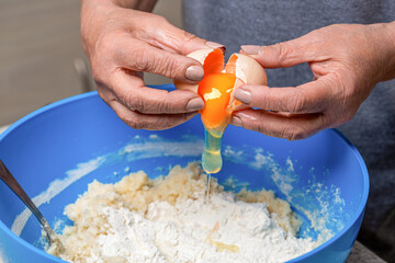 Woman breaks egg above flour to make dough. Male hand breaks egg into flour while making dough. Closeup of chef's hand with yellow egg yolk in preparation process for baking. Hand, egg in bowl