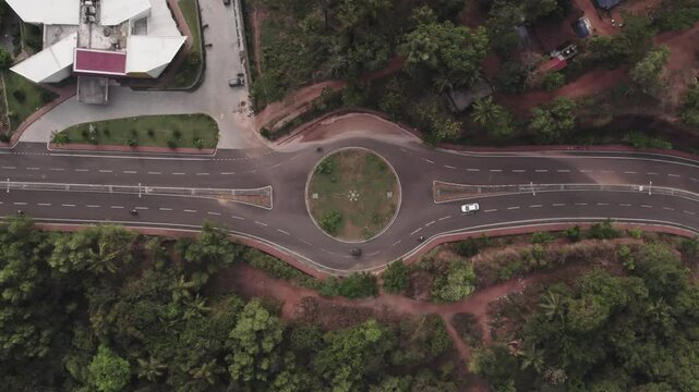 4K aerial shot or top view of traffic on roundabout intersection with slow moving car. Calm and peaceful junction with an industrial building nearby.