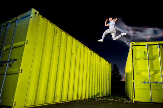 Young man free running over green cargo containers at dusk