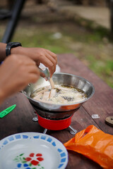 A man's hand frying sausages on a portable cooker while camping in a forest cabin, travel concept.