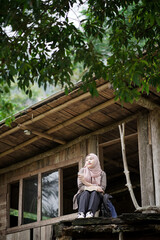 Fototapeta premium young Indonesian woman in hijab reading a book while enjoying nature in a forest cabin, travel concept.