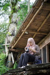 young Indonesian woman in hijab taking nature scenery photo from forest cabin, travel concept.
