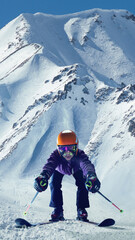 Skier leaning forward with ski poles on snowy slope, surrounded by towering mountain peaks under...