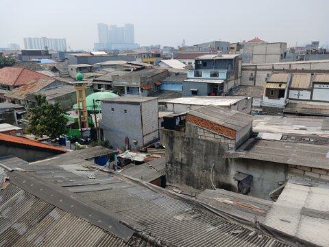 JAKARTA, INDONESIA - OCTOBER 2026: Aerial view of densely populated residential neighborhood with house rooftops and a neighborhood mosque under hazy sky.