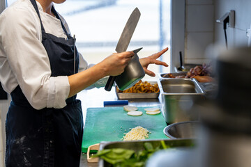 Dans les cuisines d'un restaurant étoilé, préparation d'un plat à base de légumes et fruit de mer. Découpe des légumes par le chef avec un couteau japonais.