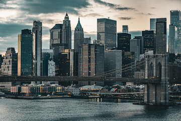 Obraz premium Die Skyline von Manhattan mit der ikonischen Brooklyn Bridge bei Dämmerung. Wolkenkratzer, sanftes Licht und der East River spiegeln die dynamische Eleganz von New York City wider.
