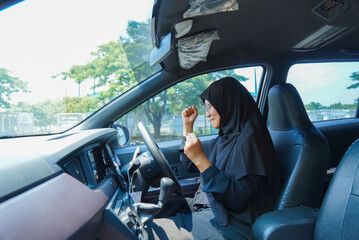 A woman in a black hijab is driving a car. She is holding her hands up in the air