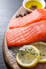Pieces of fresh salmon with thyme, lemon, oil and spices on black table, closeup