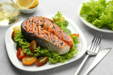 Tasty grilled salmon steak with vegetables served on light grey table, closeup