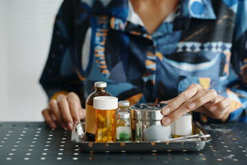 Closeup of unrecognizable female hand choosing container filled with medications while sitting at desk at home