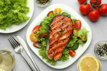 Tasty grilled salmon steak with vegetables served on light grey table, top view