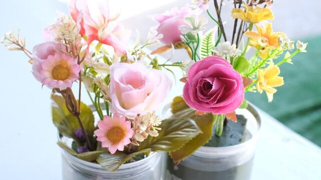Two vases of flowers, one pink and one yellow, sit on a table. The pink vase has a rose in it, while the yellow vase has a yellow flower