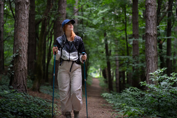 Naklejka premium Young woman tourist with backpack and walking stick hiking the forest path
