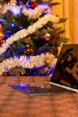 There are Christmas tree decorations, a candle and a laptop on the table. There is a Christmas tree...