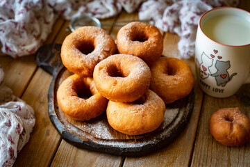 Home cooking: Donuts with powdered sugar on a wooden table. Sugar donuts for dessert. Close-up