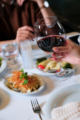 Woman Hand Holding a Glass of Red Wine at a Turkish Dining Table. The table is filled with traditional mezes, creating a cozy and elegant dining experience.