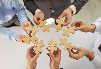 Close-up view of businesspeople hands holding wooden puzzle pieces in an office, symbolizing...