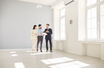 Male real estate agent in suit showing potential buyers new spacious apartment. Professional...