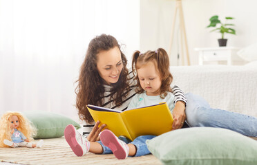 Mother and daughter enjoy quality time reading a book at home, sharing moments of happiness and...