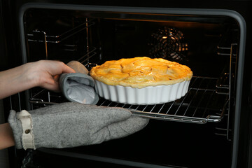 Woman putting homemade apple pie into oven in kitchen, closeup