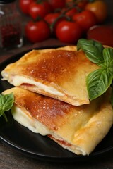 Pieces of delicious calzone pizza with mozzarella, tomatoes and basil on wooden table, closeup