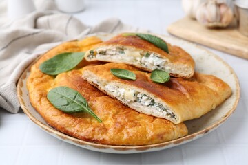 Tasty calzones with basil and cheese on white table, closeup