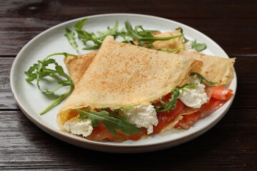 Delicious crepes with salmon, cream cheese and arugula on wooden table, closeup
