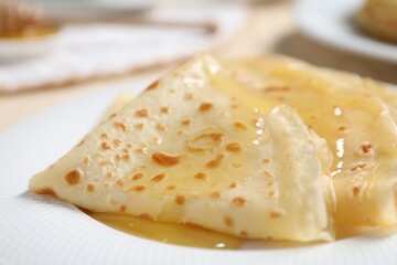 Tasty crepes with honey on plate, closeup