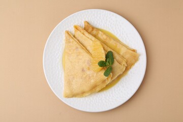 Plate with tasty crepes Suzette on beige table, top view
