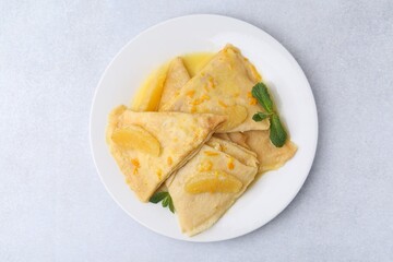 Plate with tasty crepes Suzette on light textured table, top view
