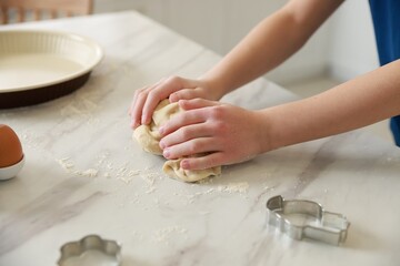 Boy kneading dough at white marble table in kitchen, closeup