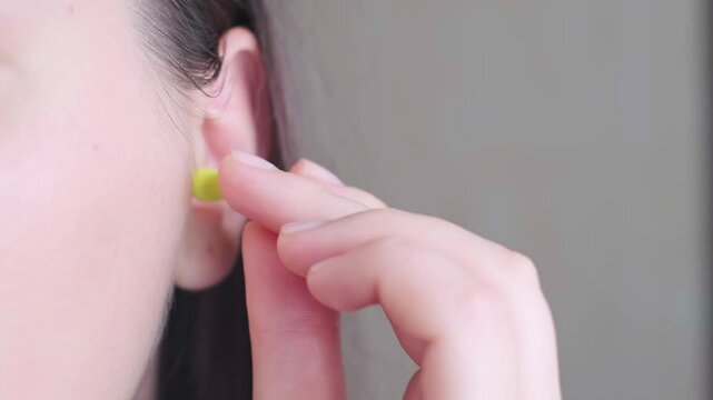 Close-up of a woman's hand squeezing earplugs before inserting them into the ear canal, preparing for sleep in a noisy city.