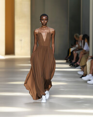 A runway model showcasing a flowing mocha mousse maxi dress with subtle draping, walking on a minimalist runway