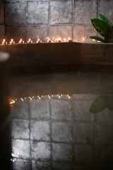 A serene spa-like setting featuring tea light candles neatly aligned along the edge of a curved concrete surface. Soft ambient lighting highlights the reflective surface of the water 